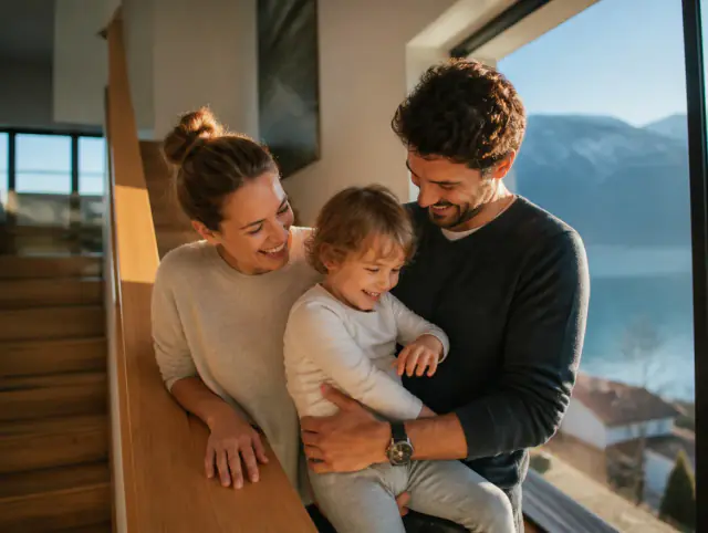 Treppengeländer aus Holz – glückliche Familie mit Kind Glückliche Familie mit Kind lacht gemeinsam an einem Treppengeländer aus Holz