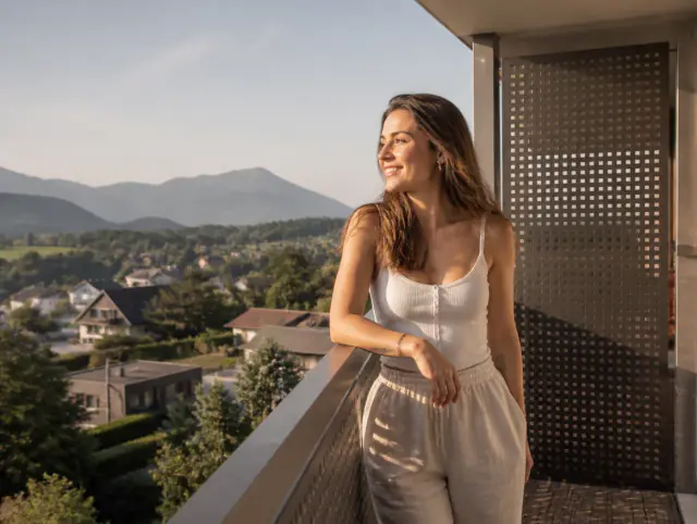 Lächelnde Frau geniesst den Ausblick an einem Balkongeländer mit Lochblech