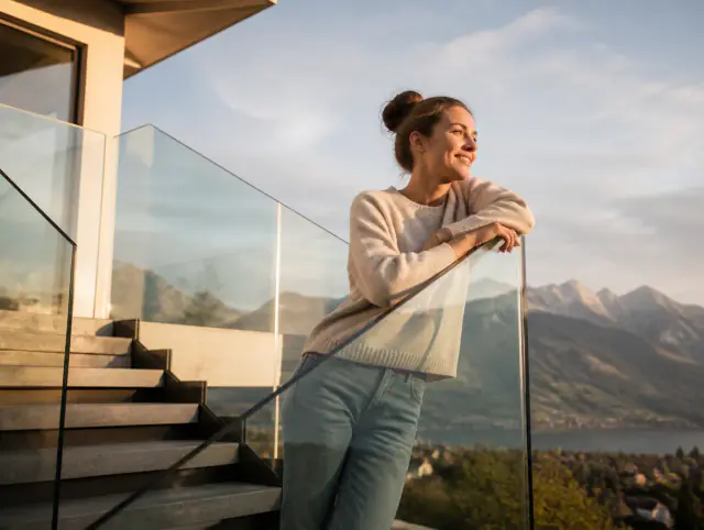 Lächelnde Frau geniesst den Ausblick an einem Glasgeländer aussen
